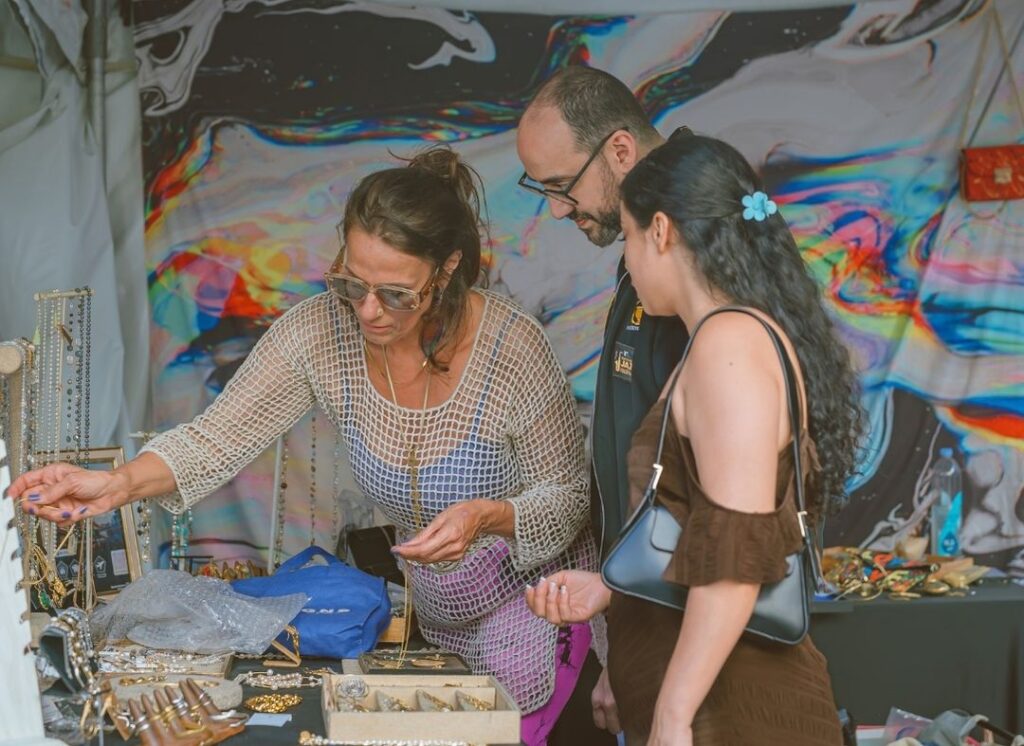 Artist showing jewelry to festival attendees inside a colorful art booth at the South Beach Jazz Festival on Lincoln Road in Miami Beach