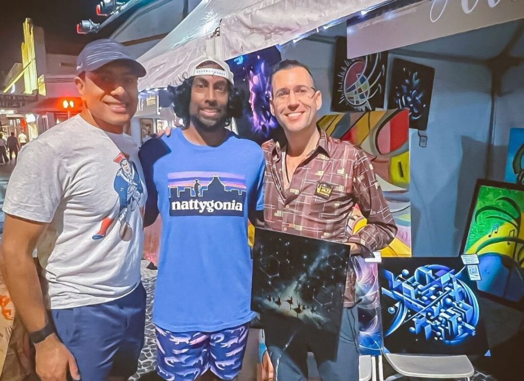 Three South Beach Jazz Festival attendees posing together in front of colorful original artwork at an artist booth on Lincoln Road in Miami Beach