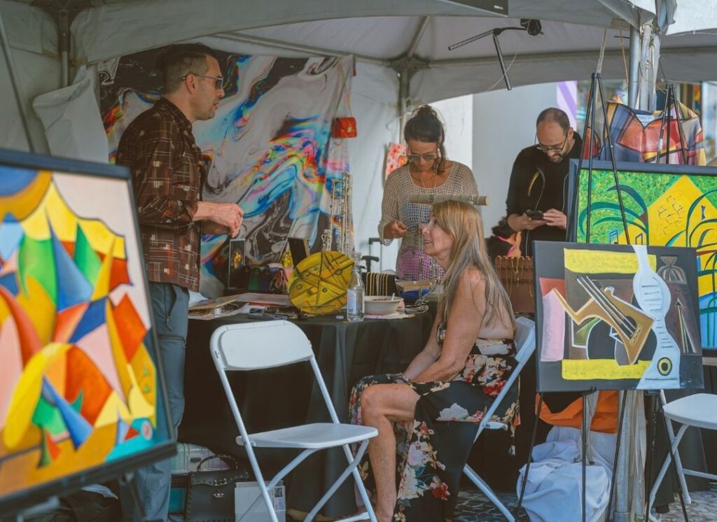 Festival attendees browsing artwork and jewelry inside a visual arts booth at the South Beach Jazz Festival on Lincoln Road in Miami Beach